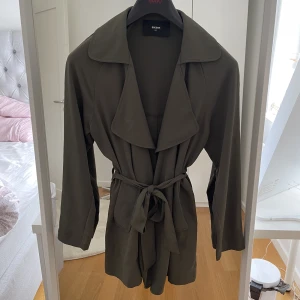 trenchcoat - Militärgrön trenchcoat ifrån Bikbok i storleken xs. Har fickor på sidorna. 