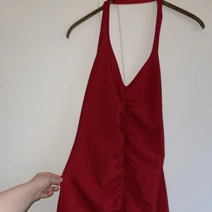 Rödglittrig klänning med halterneck - Rödglittrig kort klänning med halterneck. Formgivande och öppen i ryggen. Endast använd en gång. Superfin festklänning i superfint skick! Säljer då den aldrig kommer till användning. Hör av dig om du undrar något!