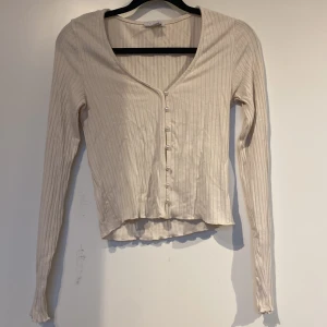 Långärmad tröja  - Obs dåligt ljus. Säljer denna tröja i färgen beige. Super stretchiga material och är ribbad. Tröjan har även pärlor längst magen som även går att knäppa upp. Köpt secondhand men har aldrig kommit till användning.