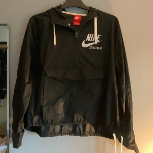 Nike vindjacka - Jag är inte den första ägaren till plagget men har själv inte haft den särskilt länge. Inga skador på plagget och allt funkar som det ska.  På bilden är sen knuten i midjan men man kan även ha den oknuten, då blir den lite längre.