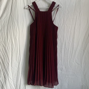 Plisserad klänning! - Vinröd plisserad klänning med axelband som korsas i ryggen, den är från NA-KD. Fin höstig färg, funkar perfekt att ha under en stickad tröja! Endast använd ett fåtal gånger och så gott som ny. 