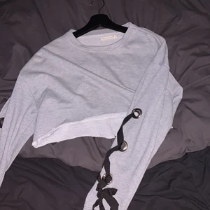 Grå tröja med snörning på armarna - Fin grå tröja med snörning på ärmarna. lite kortare i modellen men inte riktigt magtröja. superfint skick storlek M