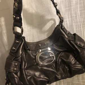 Väska Guess replika  - *många som är intresserade, kör en budgivning istället!!*  Snygg Guess axelremsväska med en super unik färg och silvriga detaljer. Finns ytterligare fack där bak. Kan mötas upp i slussen/Tcentralen annars står köparen för frakt. 