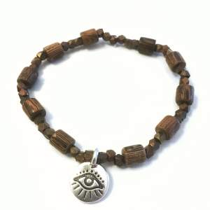 Handgjort (av mig) armband med pärlor i trä och brons, samt ett Evil Eye-hänge pläterat i antikt silver. Armbandet är elastistiskt och har en omkrets på ca 18 cm. 🤎