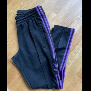 Adidas byxor - Adidas mjukis byxor, med lila rand, fickor och dragkedja vid anklarna. I god skick!