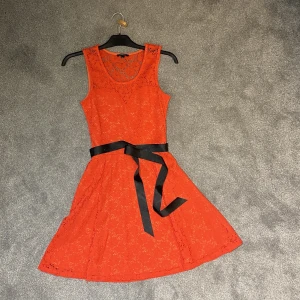 Korallfärgade spets klänning  - Söt klänning i kort modell med svart sidenband. Dragsko i sidan. Använd endast en gång.