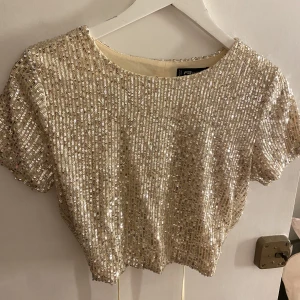 Glittrig topp - Säljer denna guld/glittriga topp i M. Toppen är öppen i ryggen och har knytning runt midjan. Den är i nyskick och säljes för 70kr+frakt🌸