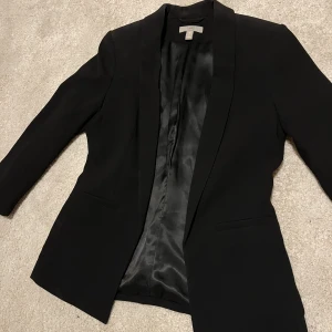 Slimfit kavaj - En svart kavaj från H&M med trekvartslånga armar och figursydd passform, formar sig så snyggt i midjan! Denna är i strl 34 och i väldigt bra skick 😊 (säljer även dem gråa kostymbyxorna på bilden)