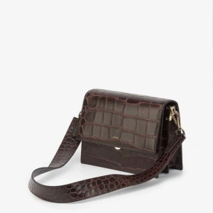 JW pei mini flap crossbody väska brown croc - Säljer min fina crossbody-väska från Jw Pei i veganskt skinn/konstläder. Aldrig använd och med lappar kvar. Avtagbar axelrem. Nypris ca 750 kr.  Väskan mäter 20cm x 15.5cm x 8cm och bandet är ca 43 cm