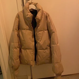Puffer - Snygg kort puffer i beige färg. Mudd vid ärmen, går att dra åt vid midjan. Passar från stl XS -M. Varm och inte använd. Köpt från New Yorker. 