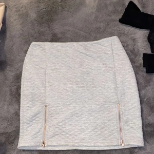 Grå kjol från Rebecca Stella - Fin kjol med dragkedjor, dragkedjorna på framsidan går att dra upp💕 säljer då jag aldrig använt den💕 Rebecca  Stellas kollektion från Nelly  Lite liten i storlek enlig tmig, så passar M-L💕 