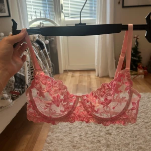 Rosa blommig spets-bh - Säljer en rosa bh med blommigt spetsmönster. Den har justerbara axelband och ryggband och är aldrig använd.