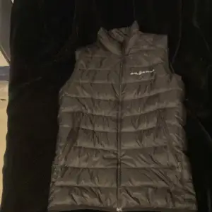 Snygg svart dunväst från Sail Racing med dragkedja framtill. Perfekt för kyligare dagar och har en stilren design med logotypdetaljer. Västen är lätt och bekväm att bära. Vid minsta intresse är det bara att skriva!