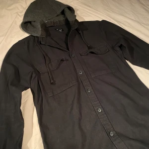 Overshirt - Säljer denna overshirt med luva ifrån pull and bear i storlek M. Jävlit najs och är perfekt att ha under en tunnare jacka nu inför vintern. Skicket är utmärt, har inga defekter eller fläckar men märker ändå att den inte är ny. Allmänt 8,5/10 har du några frågor är det bara att höra av sig!