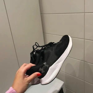 Träningsskor Under Armour - Snygga svarta skor för träning från Under Armour med vit sula och snörning. Perfekta för träning eller vardagsbruk. Stilren design med märkets logga på sidan.