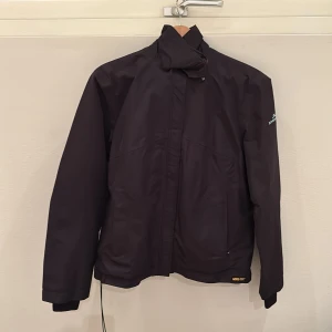 Svart regnställ goretex från J.Lindeberg - Svart regnställ (Gore tex)  från J.Lindeberg med hög krage och dragkedja. Perfekt för golf eller promenad i lite dåligt väder.