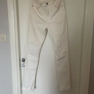 Vita jeans med slits - Snygga vita jeans med hög midja och slits vid anklarna. Perfekta för en stilren look. De har en klassisk femficksdesign och knappgylf.