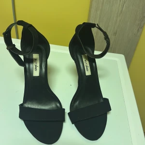 Svarta klackskor från NLY Shoes - Eleganta svarta klackskor från NLY Shoes med öppen tå och justerbart spänne runt ankeln. Perfekta för en stilren look.