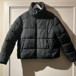 Svart pufferjacka från 157 - Snygg svart pufferjacka från 157 i storlek S. Jackan har en hög krage och dragkedja framtill. . Quiltade designen och lös passform. Mkt lätt