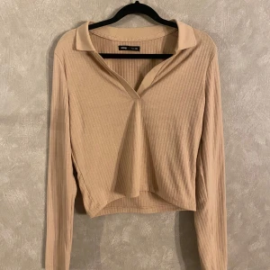 Beige ribbad topp från Sinsay - Säljer en snygg beige ribbad topp från Sinsay. Den har en v-ringad design med krage och långa ärmar. Perfekt för en stilren look.står storlek xl, men passar mig som har storlek s/m😊