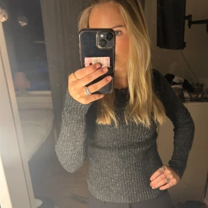 Glittrig svart tröja från H&M - Säljer en snygg glittrig svart tröja från H&M. Tröjan har en tight passform och långa ärmar, perfekt för att ge lite extra stil till din outfit. Den är tillverkad i ett bekvämt material som passar bra för både vardag och fest. Jag har sytt om den i midjan, armarna och baksidan så det inte längre finns några slittar🤗 