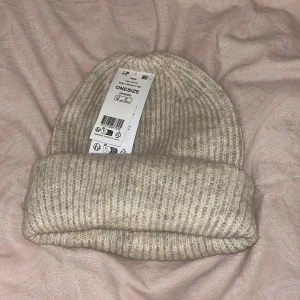 Beige stickad mössa - Helt ny Snygg beige stickad mössa i ribbat mönster. Perfekt för kyliga dagar och ger en stilren look. Passar de flesta tack vare one size-storleken.