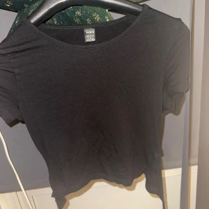 Svart kortärmad topp från Shein - Säljer en enkel och stilren svart kortärmad topp från Shein. Perfekt för en avslappnad look. Toppen har en rund halsringning och är gjord i ett mjukt material. Finns en knytning i ryggen som man ser på sista bilden 