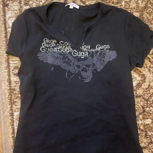 Svart t-shirt med tryck från Guga Jeans - Snygg svart t-shirt med, T-shirten har en v-ringad hals och korta ärmar. Passar storlek s och xs också!