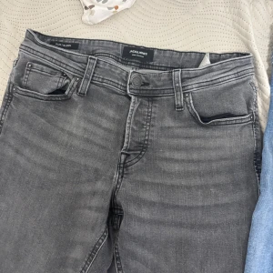 Grå jeans från Jack & Jones - Snygga grå jeans från Jack & Jones i modellen Slim Glenn. De har en slim passform och klassisk femficksdesign med knappgylf. Perfekta för en stilren look.