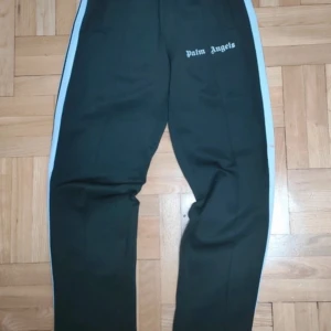 Svarta byxor från Palm Angels - Snygga svarta byxor från Palm Angels med vita sidoremsor. Byxorna har en normal passform och är tillverkade av en bomulls- och polyesterblandning för extra komfort. Perfekta för en avslappnad stil.