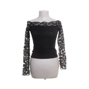 Desing by si spetstopp - Elegant svart blus med spetsdetaljer och offshoulder-design.