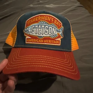 Flerfärgad keps från Stetson - Snygg keps från Stetson med broderad logga på framsidan. Kepsen har en röd skärm, blå front och orange mesh baktill för bra ventilation. Perfekt för en avslappnad stil.