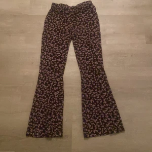 Blommiga byxor från Lindex - Säljer ett par svarta byxor med blommigt mönster från Lindex. Byxorna har en loose passform och är perfekta för en avslappnad stil. De är tillverkade i ett mjukt material som ger en bekväm känsla hela dagen.