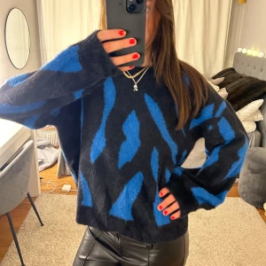 Svart och blå tröja från VILA - Säljer en snygg och mysig svart tröja från VILA med blått mönster. Tröjan har långa ärmar och en avslappnad passform. Den är gjord i ett mjukt material som känns skönt mot huden😊