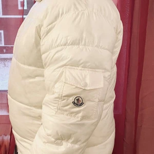 Moncler - Säljer en stilren vit dunjacka från Moncler. Jackan har en dragkedja framtill och praktiska fickor med dragkedjor. Den är perfekt för kyliga dagar och har en klassisk pufferdesign med Monclers logotyp på ärmen. Givetvis äkta men inget kvitto eller bag kvar dessvärre. Passar L/XL 