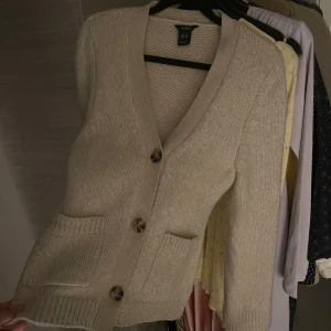 Beige stickad kofta från Lindex - Mysig beige stickad kofta från lindex med knappar framtill och två fickor. Perfekt för kyliga dagar och enkel att matcha med olika outfits. Knappt använd och köptes för 499