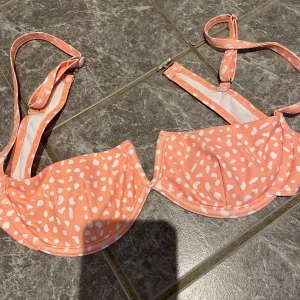 Prickig bikiniöverdel - Snygg ljus rosa/orange bikiniöverdel med vita prickar. Den har justerbara axelband och en bygel för extra stöd. Använd fåtal gånger