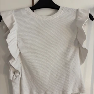 Vit ribbad topp från Zara - Säljer en vit ribbad topp från Zara med volangdetaljer på ärmarna🤩