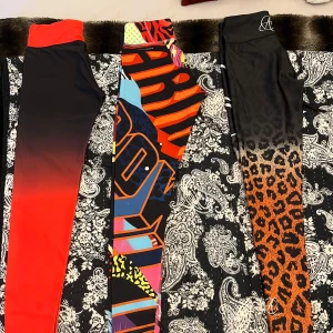 Färgglada leggings i olika mönster - Tre par leggings med unika mönster. Ett par i röd och svart ombre med texten 'Six Deuce', ett par med färgglatt abstrakt mönster, och ett par med leopardmönster som övergår i svart. Perfekta för att sticka ut! 500kr för alla tre!