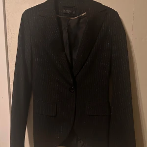 Svart randig kavaj från Topshop - Elegant svart kavaj från Topshop med diskreta ränder. Perfekt för en stilren look. Kavajen har en klassisk krage och knäppning framtill. Passar utmärkt för både formella och semi-formella tillfällen.