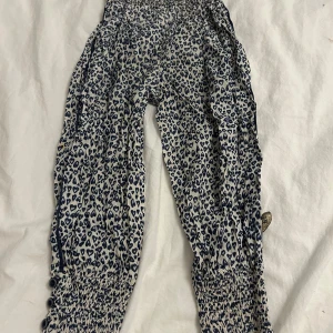 Mönstrade byxor från Little Pomp de Lux - Säljer ett par mönstrade byxor från Little Pomp de Lux i storlek 104. Byxorna har ett hjärtmönster i blått och vitt med elastisk midja och benslut för en bekväm passform. De kommer tvättas och strykas innan de skickas! ⭐️