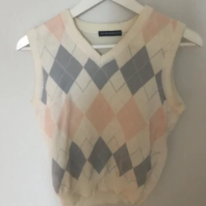 Rutig väst från Brandy Melville - Säljer en stilren väst från Brandy Melville med ett klassiskt rutmönster i grått, vitt och rosa. Västen har en v-ringad design och är perfekt för lager-på-lager-stil.