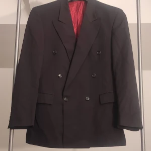 Svart kavaj från Amici i 100% ren ny ull. - Snygg svart kavaj från Amici med dubbelknäppning och klassisk design. Material: 100% ren ny ull.  Kavajen har en röd insida som ger en fin kontrast. Perfekt för formella tillfällen. 