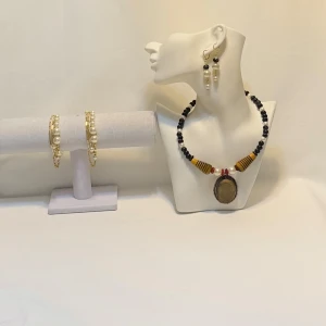 Smyckeset med pärlor och trädetaljer Jewelry A.J.D.Y  - Unikt smyckeset med ett halsband och matchande örhängen. Halsbandet har svarta och vita pärlor med stora trädetaljer och en stor medaljong. Örhängena är pärlformade med guldfärgade detaljer. Perfekt för att ge en bohemisk touch till din stil. Ett par örhängen och ett par armband plus en halsband handgjorda mycket mycket fint nytt oanvänd 