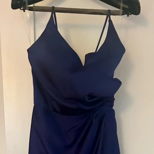 Långklänning från Cecilia Mode - Elegant marinblå långklänning med hög slits fram från Cecilia Mode med smala axelband och draperad detalj framtill. Perfekt för en stilren och klassik look. Använd 1 ggr. Nypris 2500kr