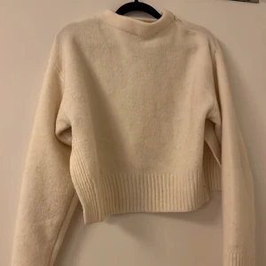 Beige stickad tröja - Säljer en mysig beige stickad tröja med ribbade detaljer vid nederkant och ärmslut. Perfekt för kyliga dagar.