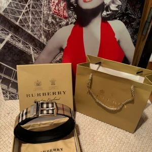 Burberry bälte - Snyggt bälte från Burberry med klassiskt rutigt mönster i beige, svart och röd. Bältet har ett stilrent silverfärgat spänne och är perfekt för att ge en touch av lyx till din outfit. Kommer med originalförpackning. Är i mycket bra skick! Det är 110 cm långt.