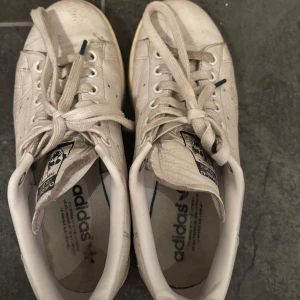 Äkta Adidas Stan Smith - Vita Adidas Stan Smith med svart och lite mörkgrönt vid det sydda märket på baksidan. Använda men har många år kvar.