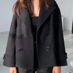 Svart kappa med knappar - Snygg svart kappa med dubbelknäppning och bred krage. Kappan har långa ärmar och stilrena knappar som ger en klassisk look. Perfekt för kyligare dagar och passar till många olika tillfällen! Den har dock tappat en utav knapparna framtill, lite torkat nagellim på högra armen längre ner vid knappen typ på armen som man ser på andra bilden och är lite nopprig annars fint skick☺️