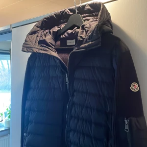Mörkblå cardigan från Moncler - Snygg svart pufferjacka från Moncler med huva och dragkedja. Jackan har långa ärmar och ett stilrent märke på ärmen. Perfekt för kyligare dagar. 